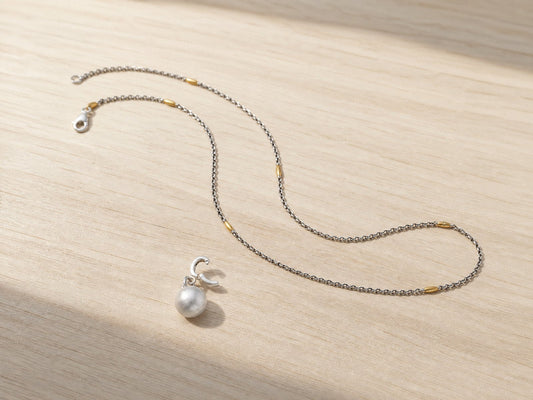 Mini silver bud charm with its clip hoop open, beside a beaded silver chain on a pale wooden table - Golden Horn Jewellery