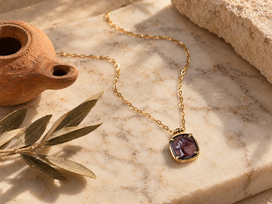Carved Nefertiti profile pendant in a gold-plated setting on a pale marble slab beside a terracotta oil lamp and olive leaves - Golden Horn Jewellery