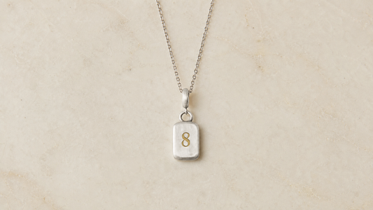 Golden Horn Number 8 numerology pendant in brushed sterling silver with a polished gold numeral, on plain cream marble