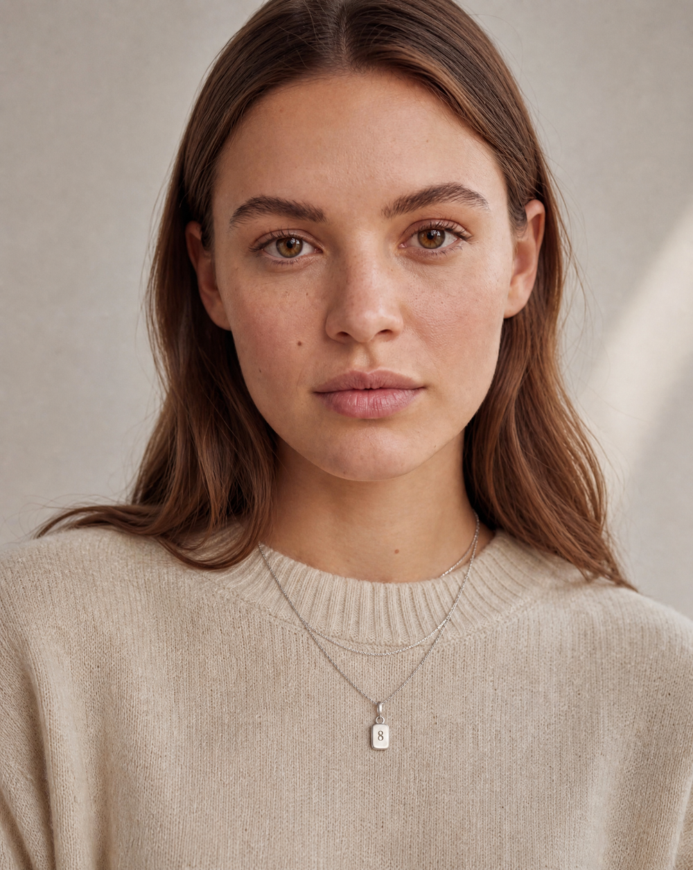 Woman wearing two layered sterling silver necklaces with a Number 8 pendant over a cream knit jumper