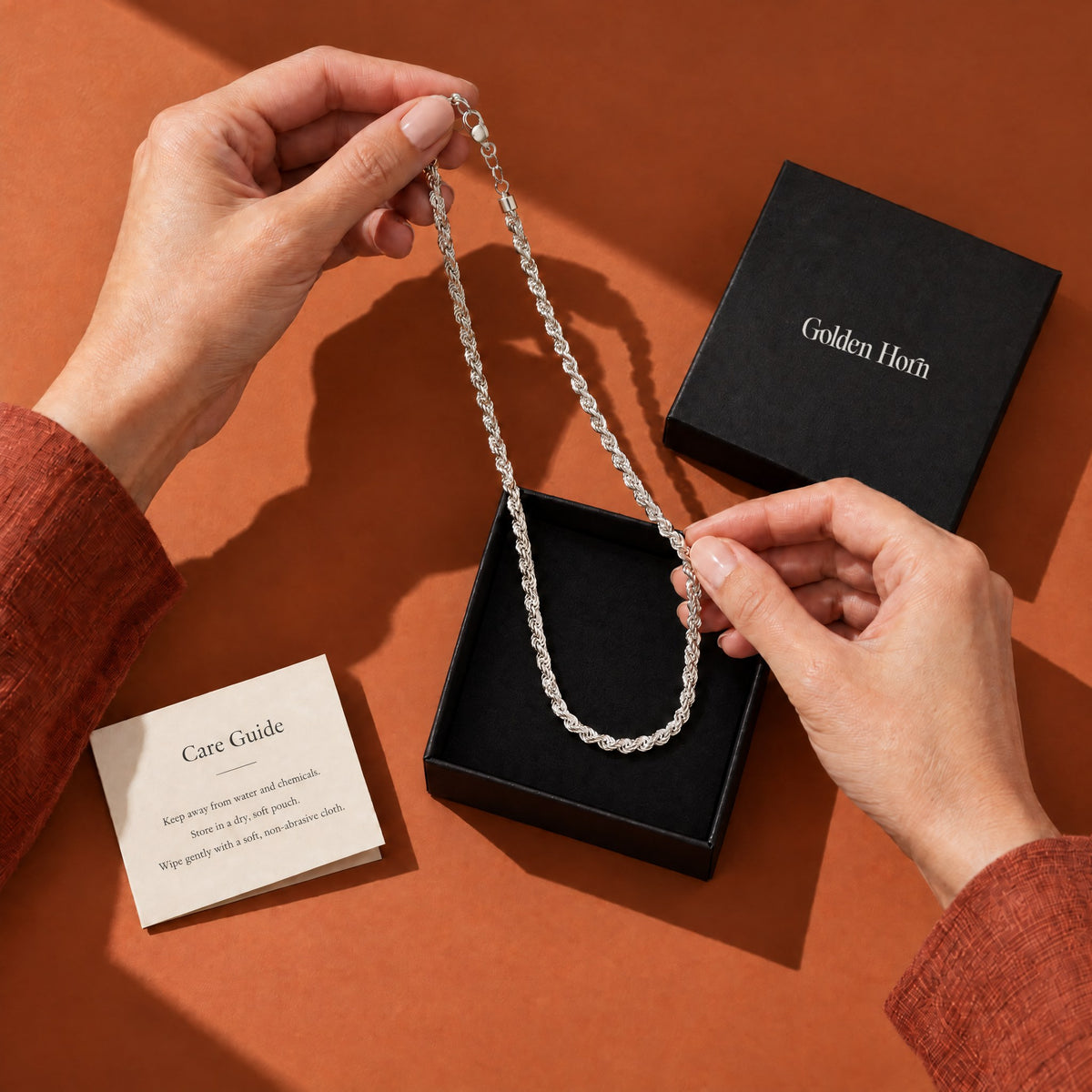 Silver rope chain being placed into a Golden Horn gift box with a care guide card