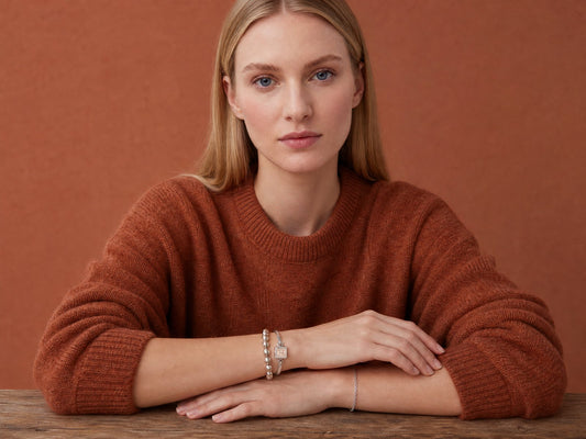 One wrist layered with a soap charm bracelet and a beaded silver bracelet, the other wearing a single fine chain - Golden Horn Jewellery