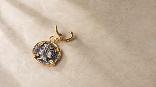 Janus coin pendant with warm gold frame and antique silver coin, on cream marble