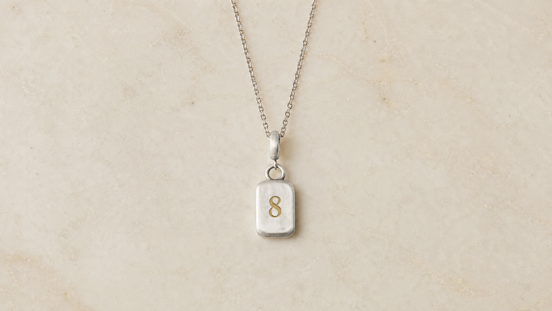 Golden Horn Number 8 numerology pendant in brushed sterling silver with a polished gold numeral, on plain cream marble