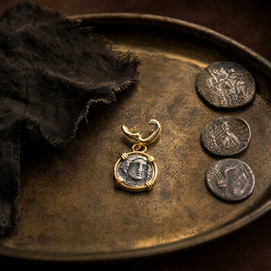 Gold-set antique coin pendant on a brass tray beside three worn ancient coins - Golden Horn Jewellery
