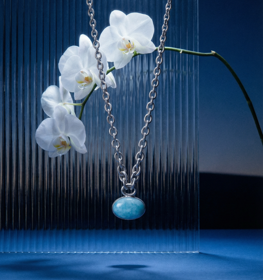 Necklace with a blue pendant hanging between white orchids against a dark background