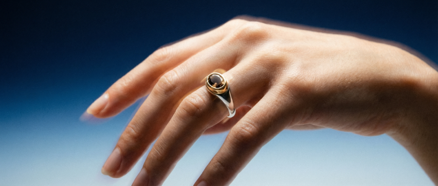 Hand wearing a ring with a dark gemstone against a gradient background