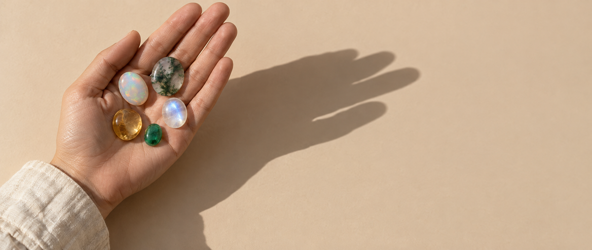 Open palm holding old-stock gemstone cabochons on a sand backdrop — Golden Horn Jewellery